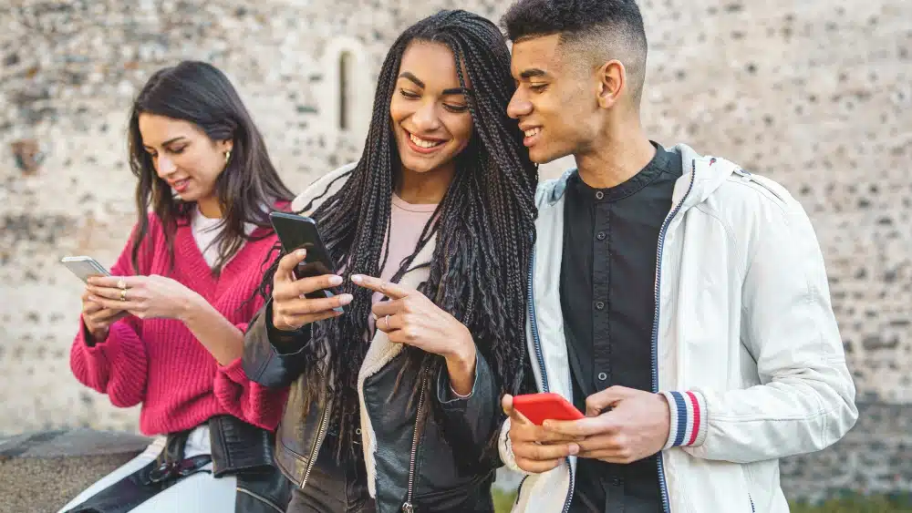 A group of three Generation Z teens show each other content on their phones. 
