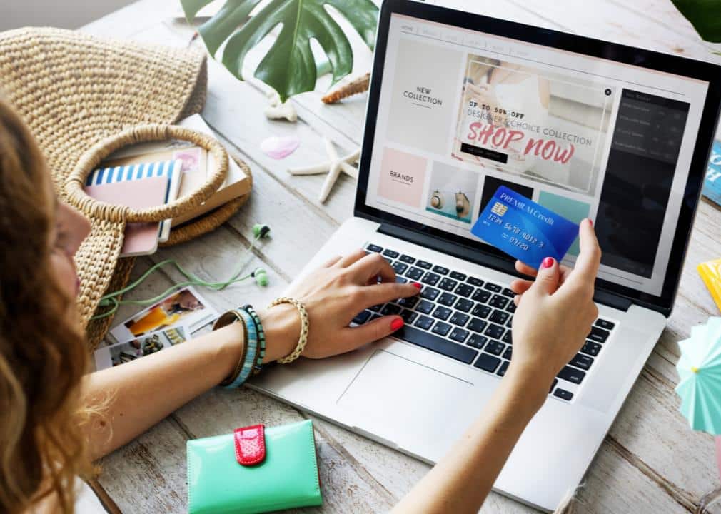 A woman shops at an online store via her laptop with a blue credit card in hand.
